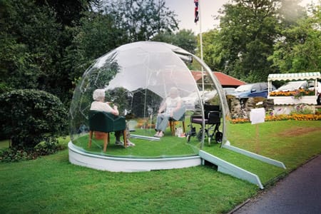 Seniors in a garden bubble pod while visit in a care home