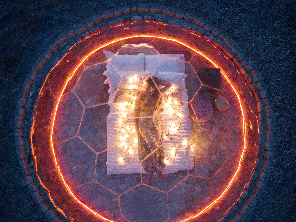 Aerial night view of a clear glamping dome bed ringed with fairy lights