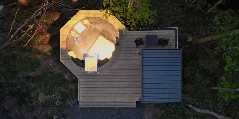 Aerial view of an opal Hypedome and timber deck glowing at dusk in the forest