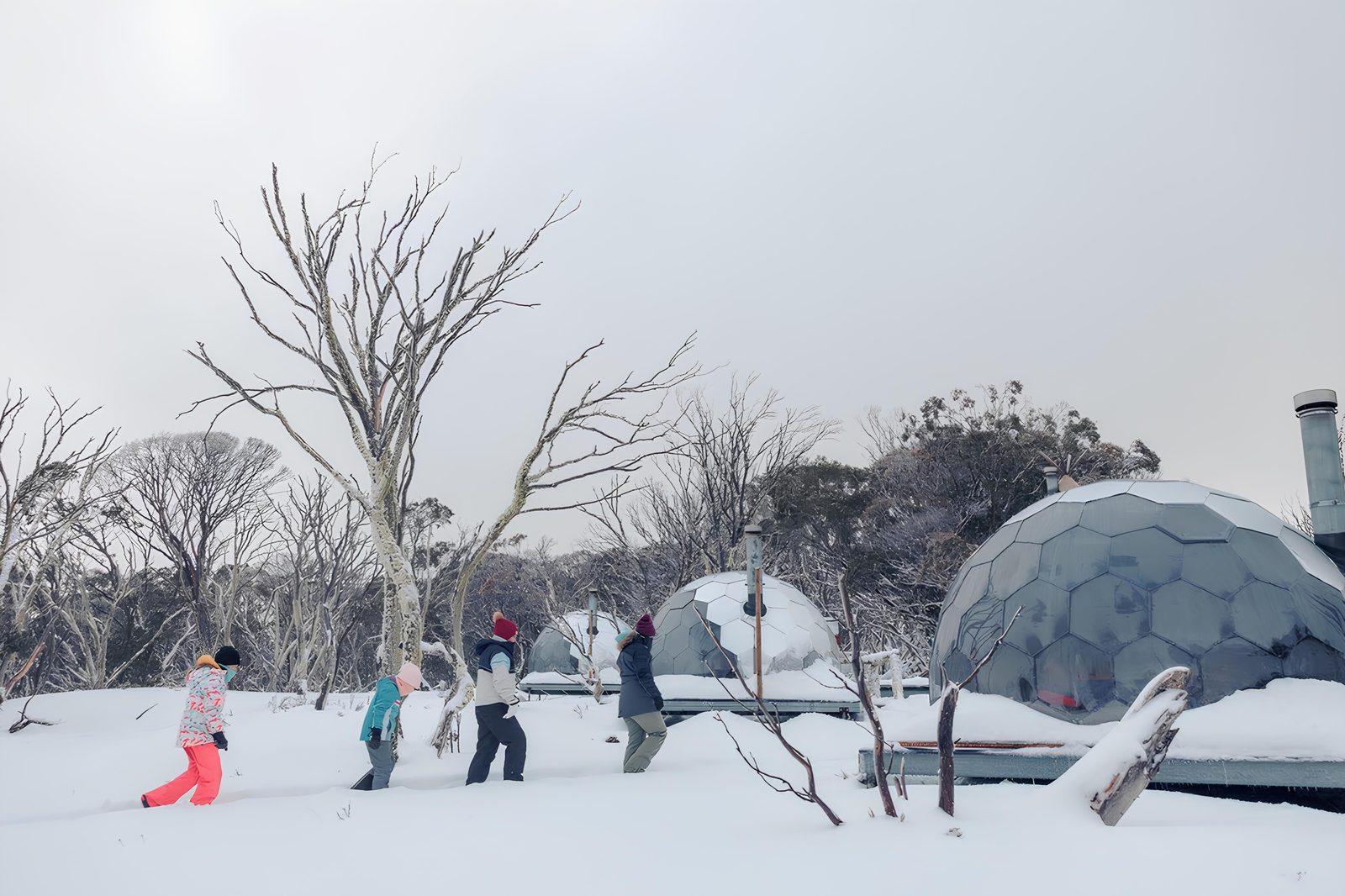 Guests walking past Hypedome glamping domes in alpine winter snow