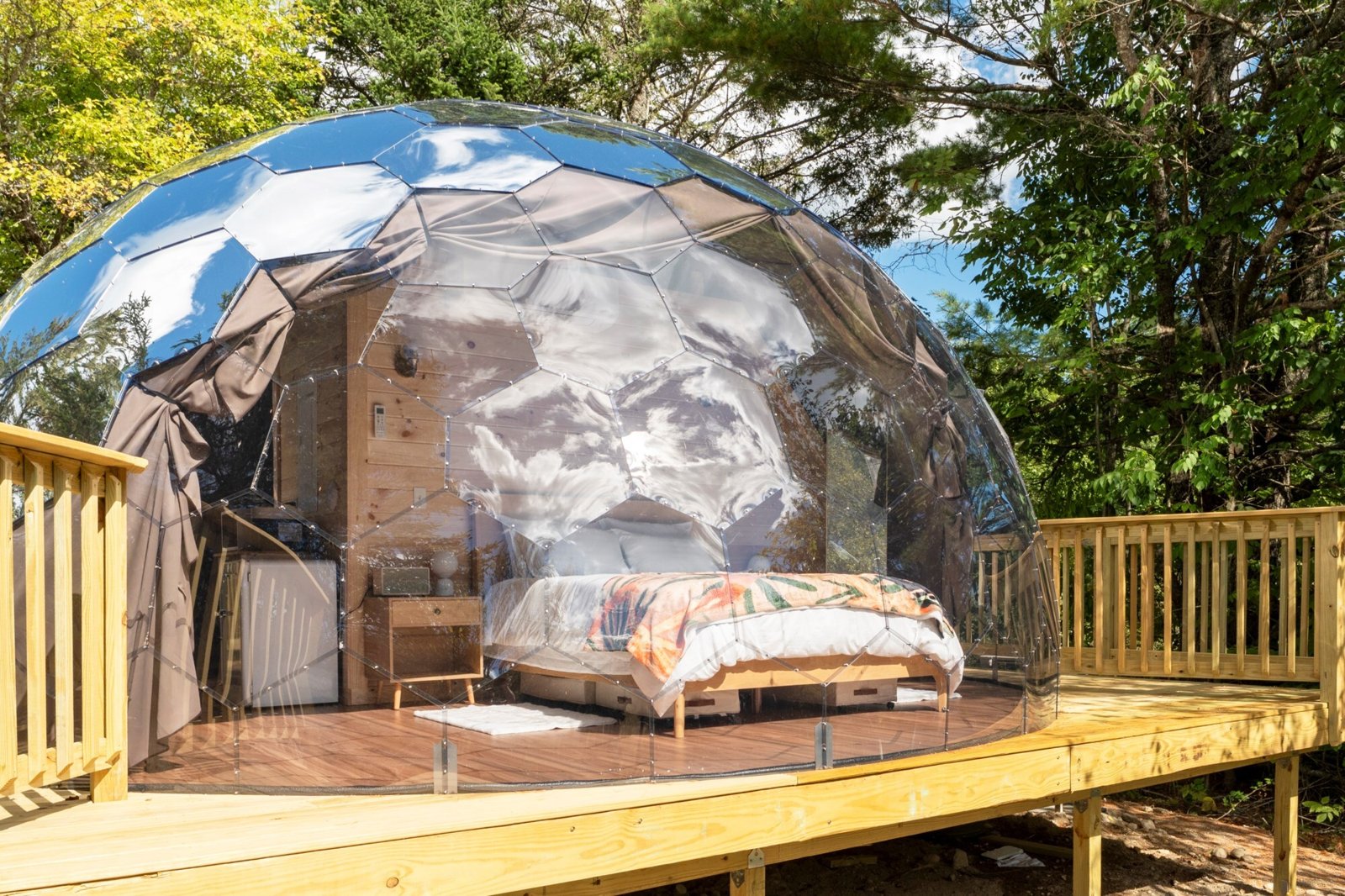 Mirror geodesic glamping dome with a bed on a forest deck