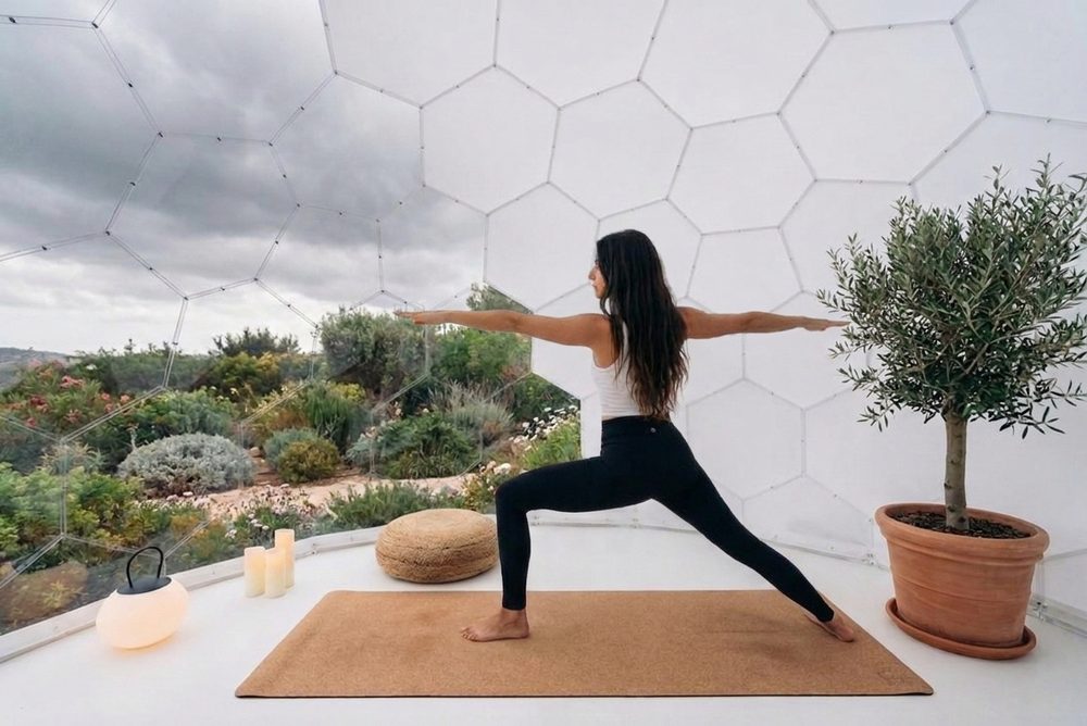 A person doing yoga stretches on a mat inside a Wellness Dome, garden visible through the clear front