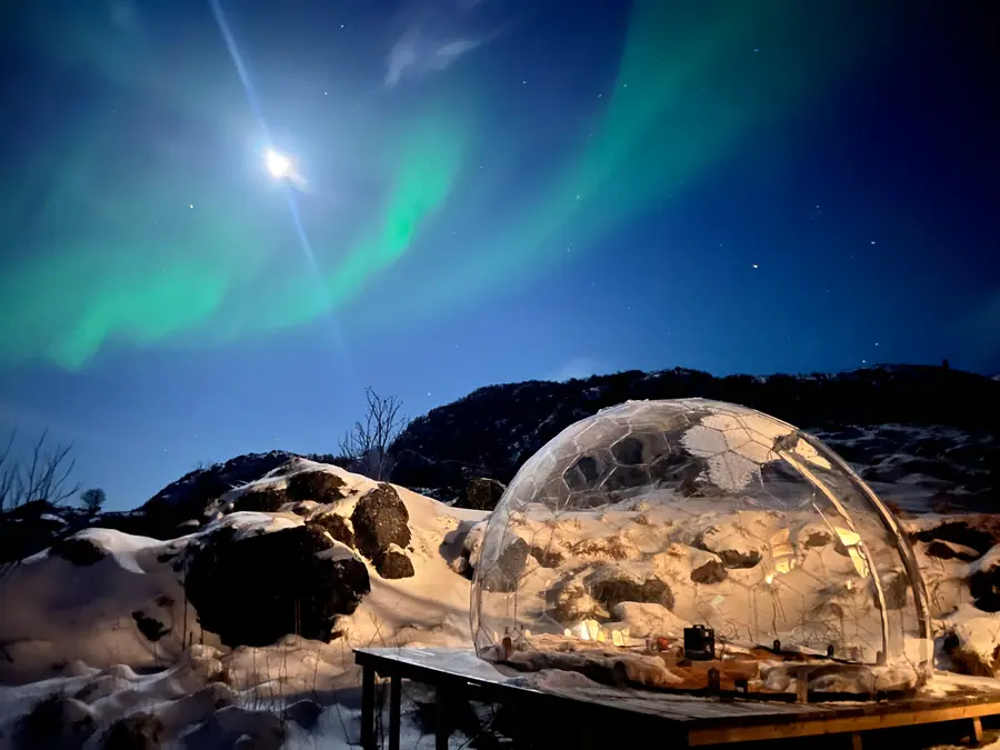 Clear dome glowing on a snowy platform under the northern lights