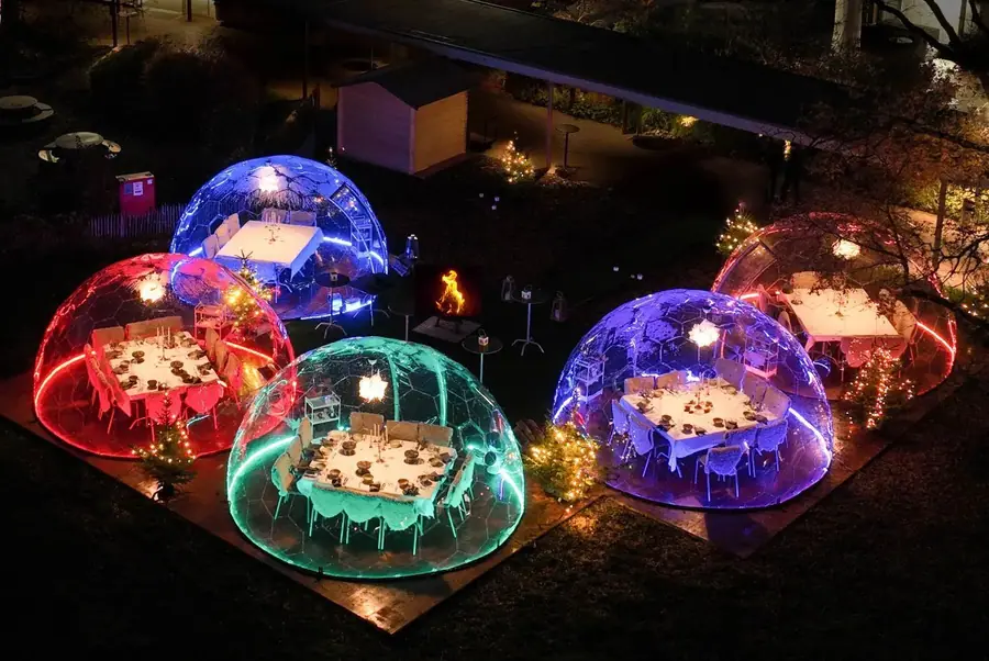 Five LED-lit dining domes set for dinner in a garden decorated with Christmas trees