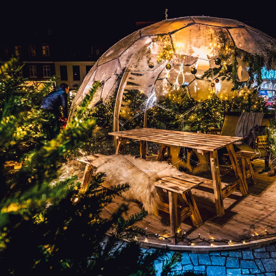 Hypedome at a Christmas market at night, decorated with fairy lights, baubles and fir branches around a wooden table