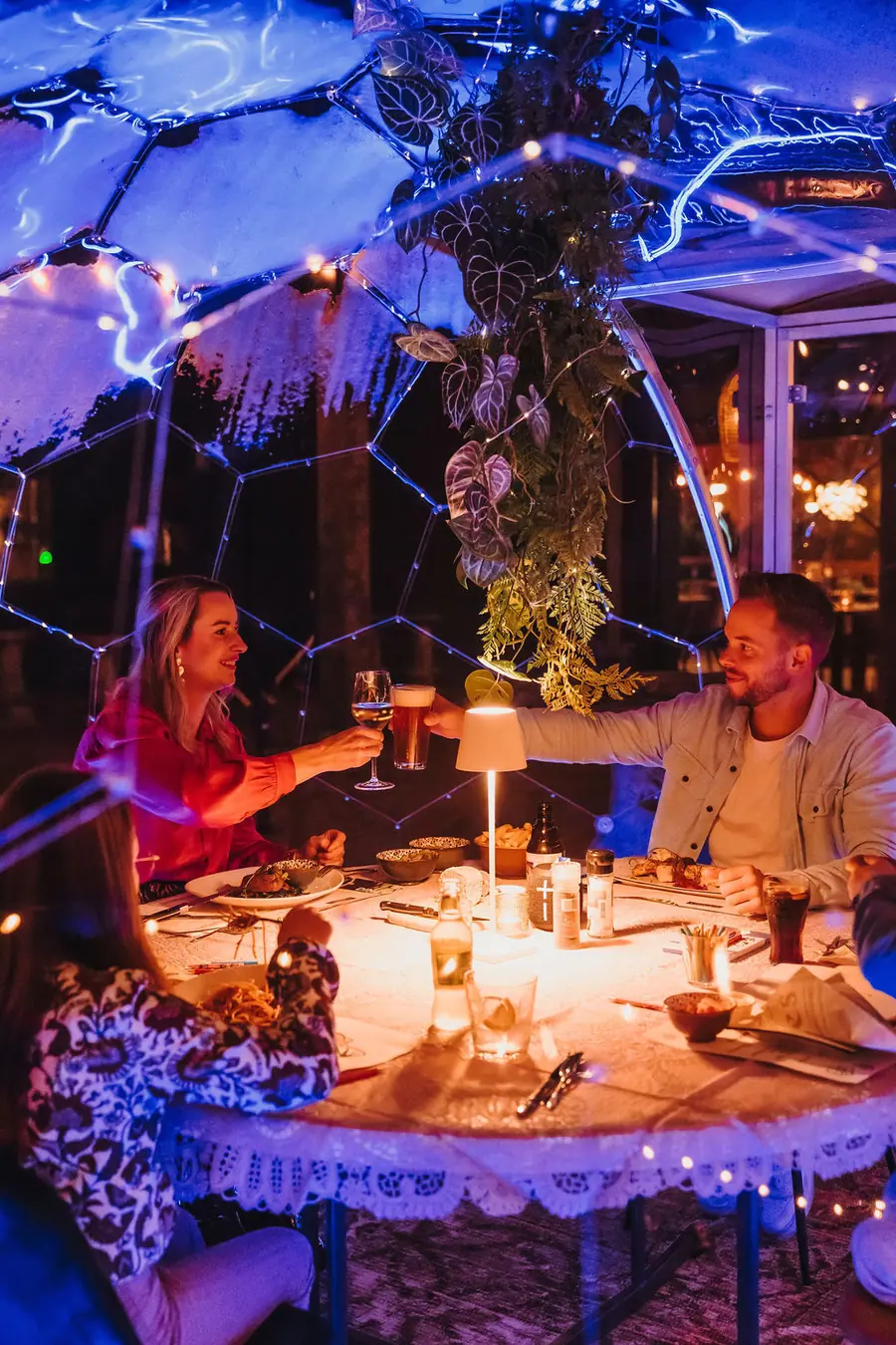 Couple toasting inside a fairy-lit dining dome at night