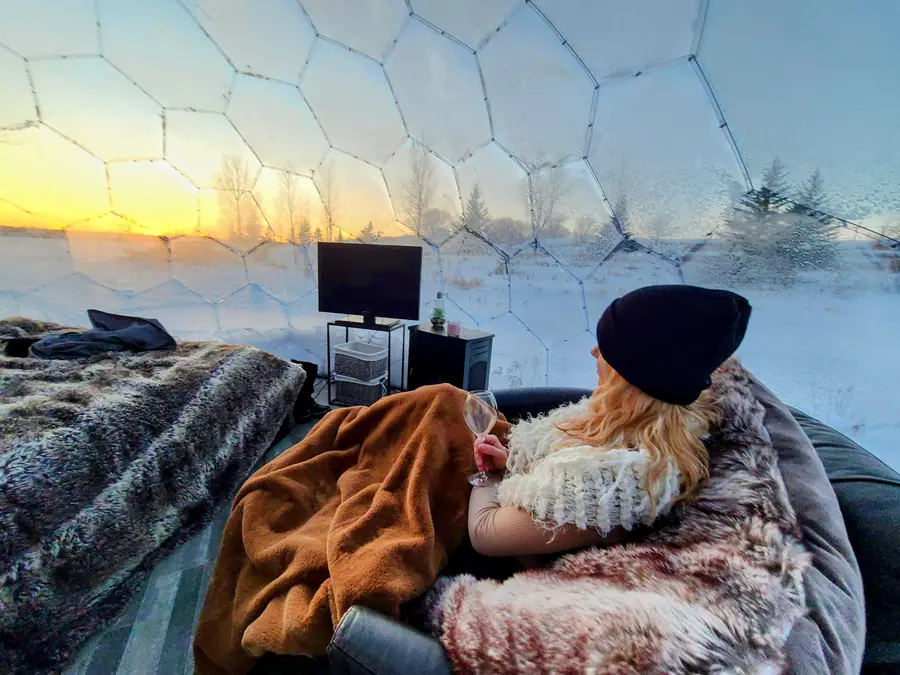 Guest wrapped in a blanket sipping wine inside a frosted dome at sunset