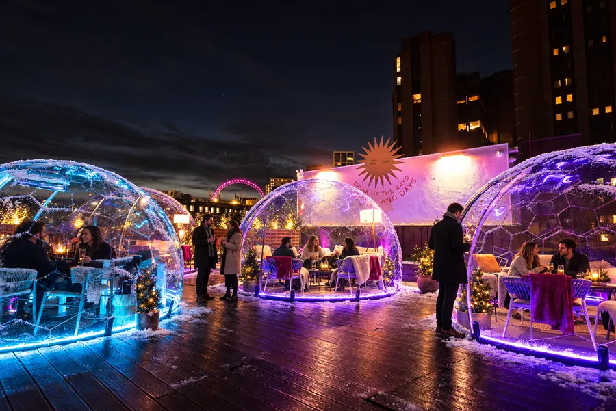 Guests dining in LED-lit domes on a rooftop bar terrace at night with the London Eye in the background