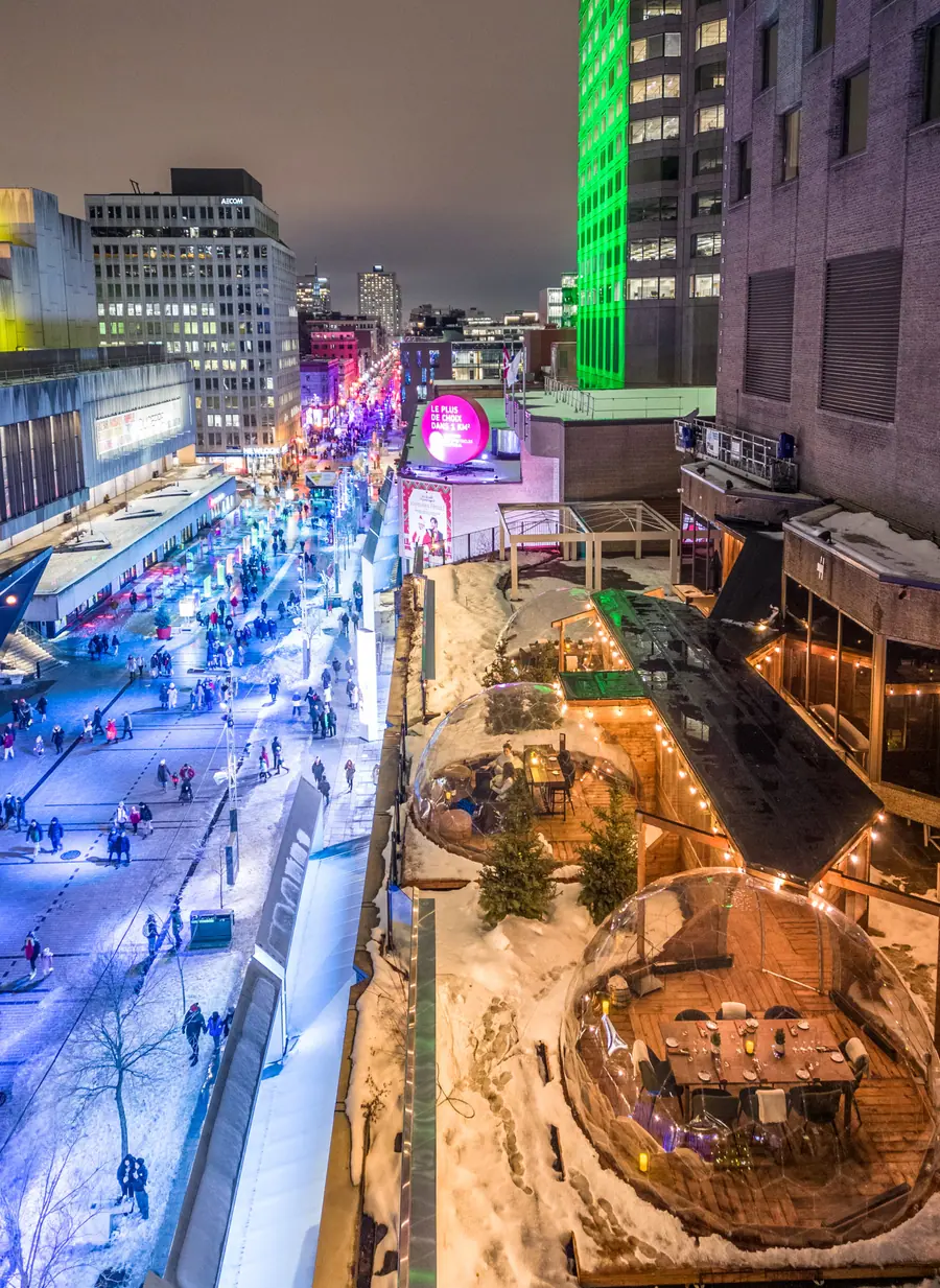 Two illuminated dining domes on a rooftop terrace above a snowy pedestrian street