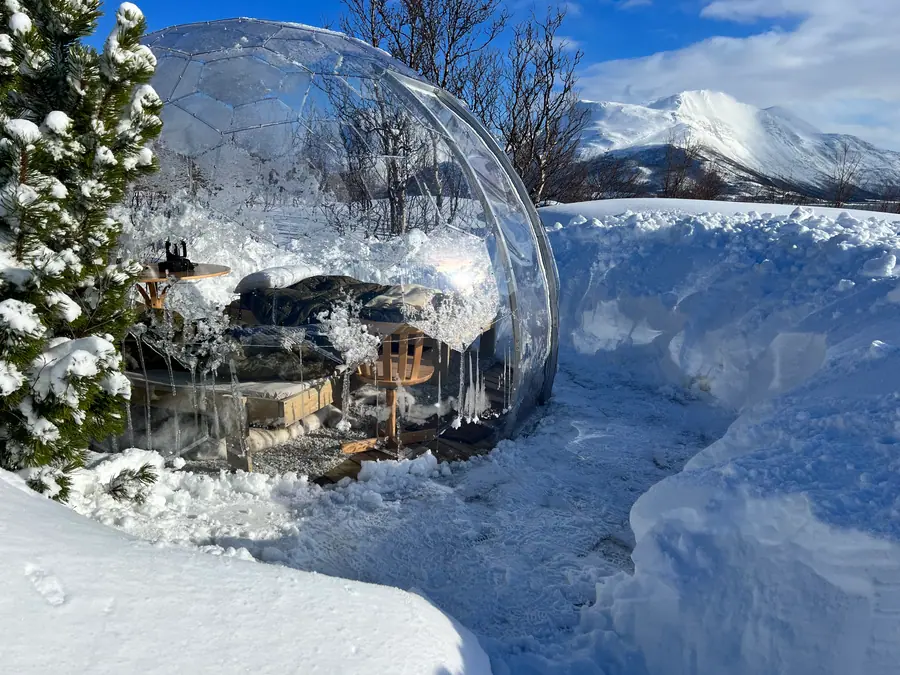 Snow-covered clear dome with icicles against snowy mountains