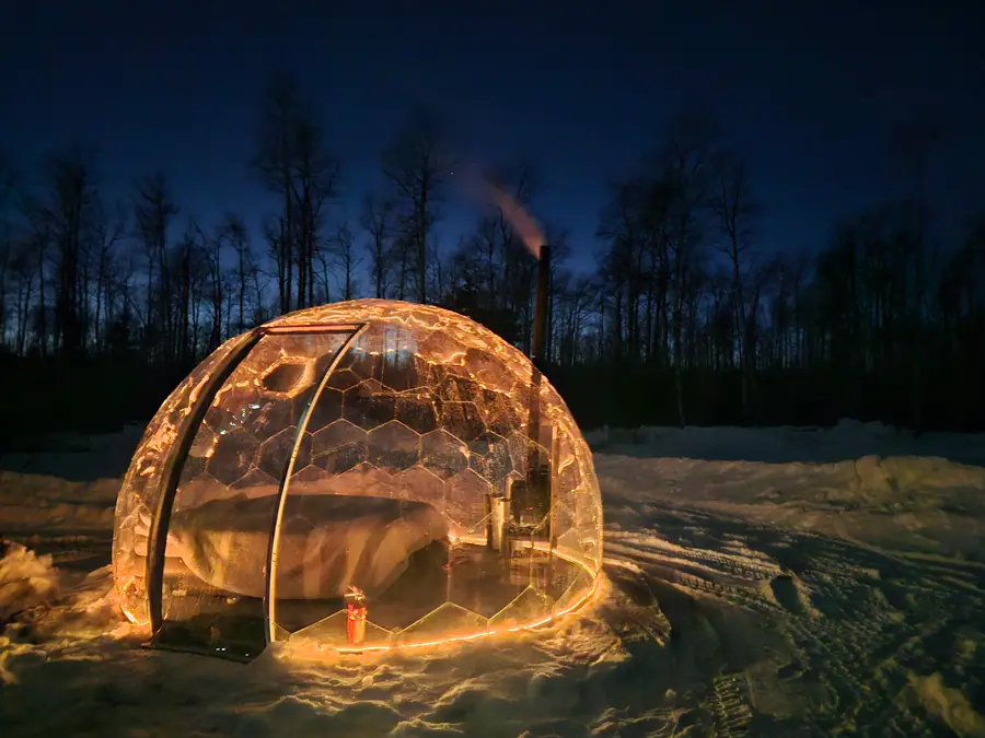 Snow-covered dome glowing at night with a wood stove inside
