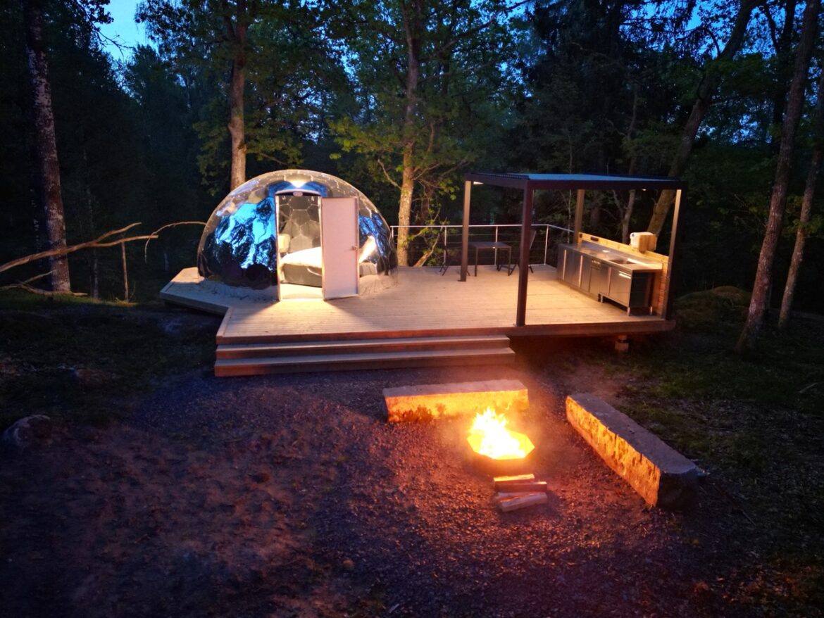 Un glamping Hypdome miroir avec porte pleine sur une terrasse avec un foyer et une kitchenette.