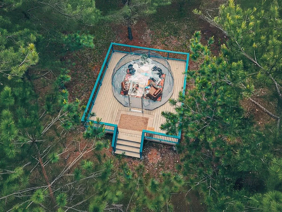 A large stargazing dome on a wooden deck surrounded by trees