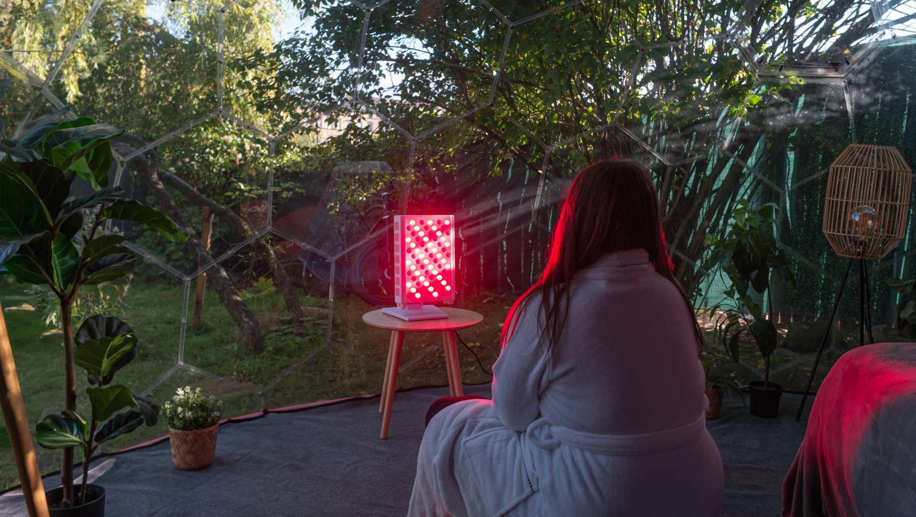Eine Frau genießt ein Rotlicht-Wellness-Ritual in einem Hypedome-Wellness-Rückzugsort im Hinterhof, der für Langlebigkeit ausgelegt ist