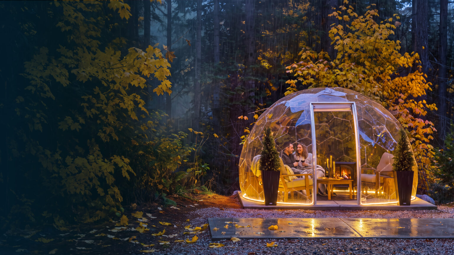 A clear Hypedome glowing with warm light in an autumn forest at dusk