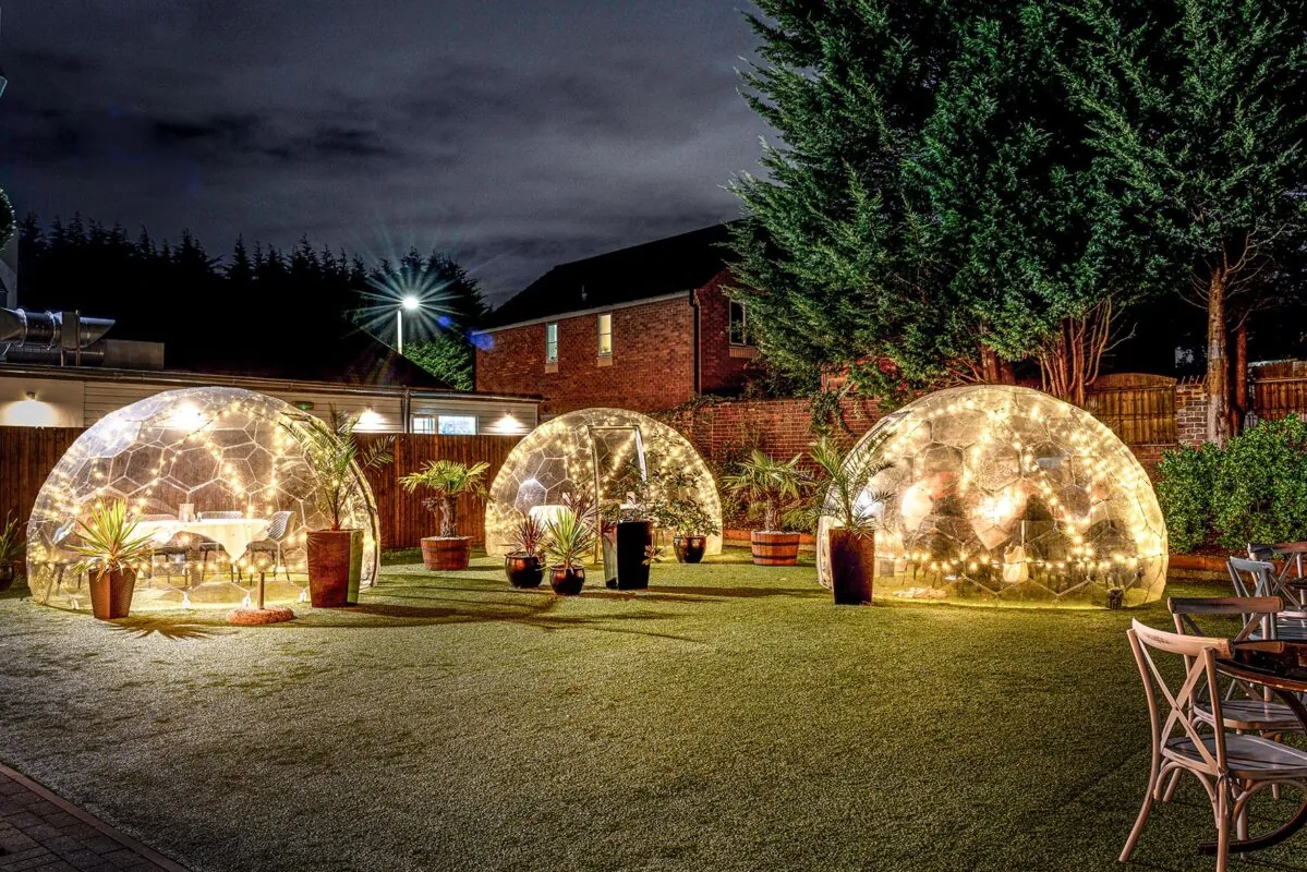 Three dining pods by night surrounded by neighbourhood houses