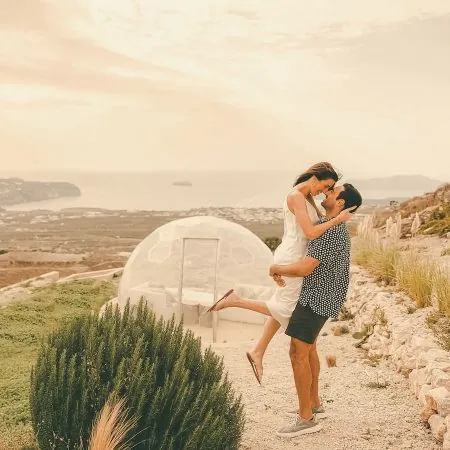A couple having a great time together, with an outdoor dome and the sea behind them