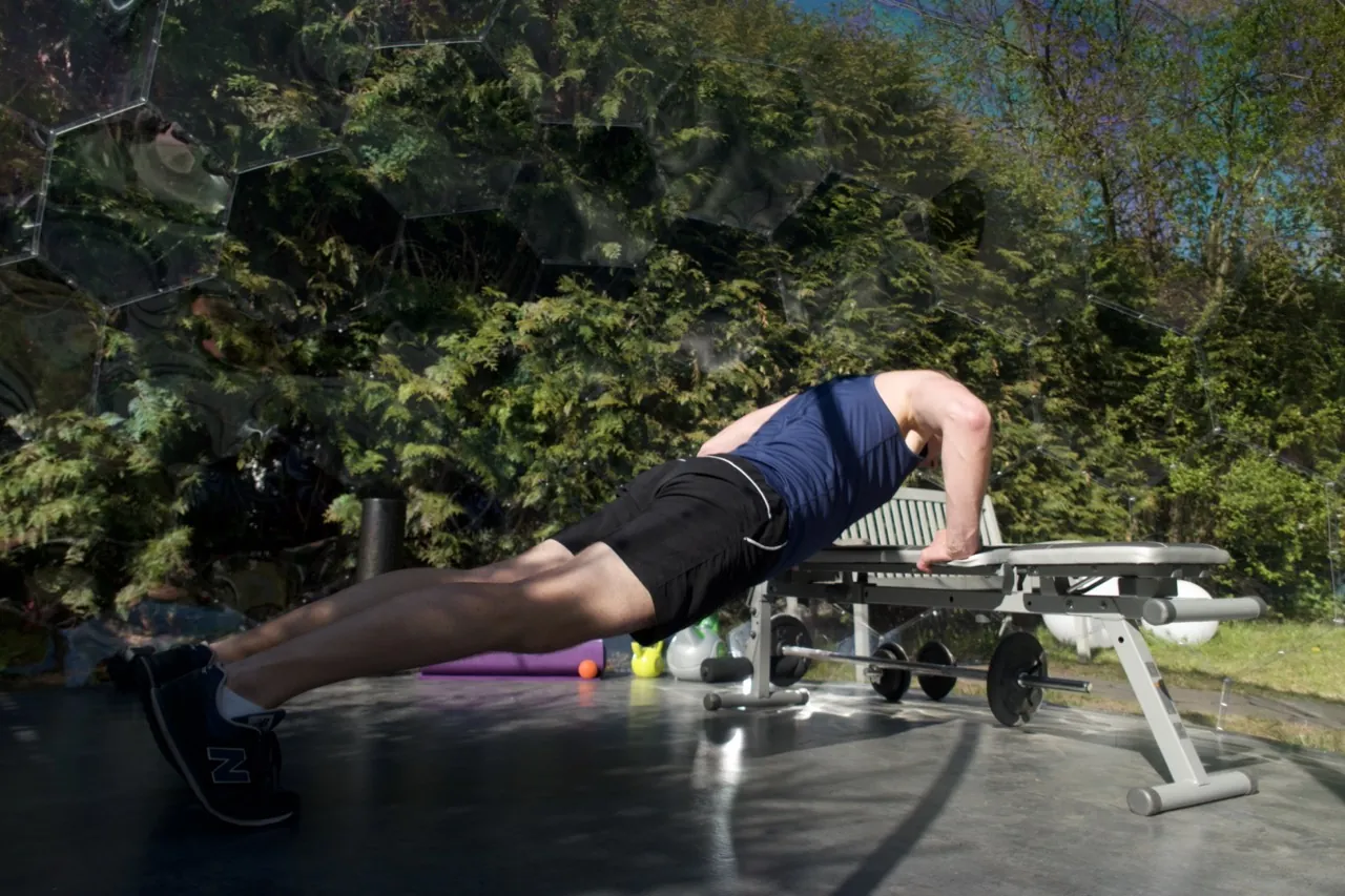 A man working out in an outdoor gym in a garden pod