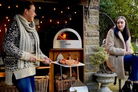 Two women making a pizza in an outdoor oven in the winter patio