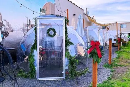 Dining pods decorated with a Christmas spirit, with wreaths, tree branches, red ribbons and bells