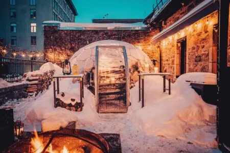 A dining dome decorated for winter time, covered in snow, with a fire pit burning outside.