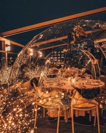 Dining pod in a rooftop restaurant under the midnight sky, illuminated by fairy lights