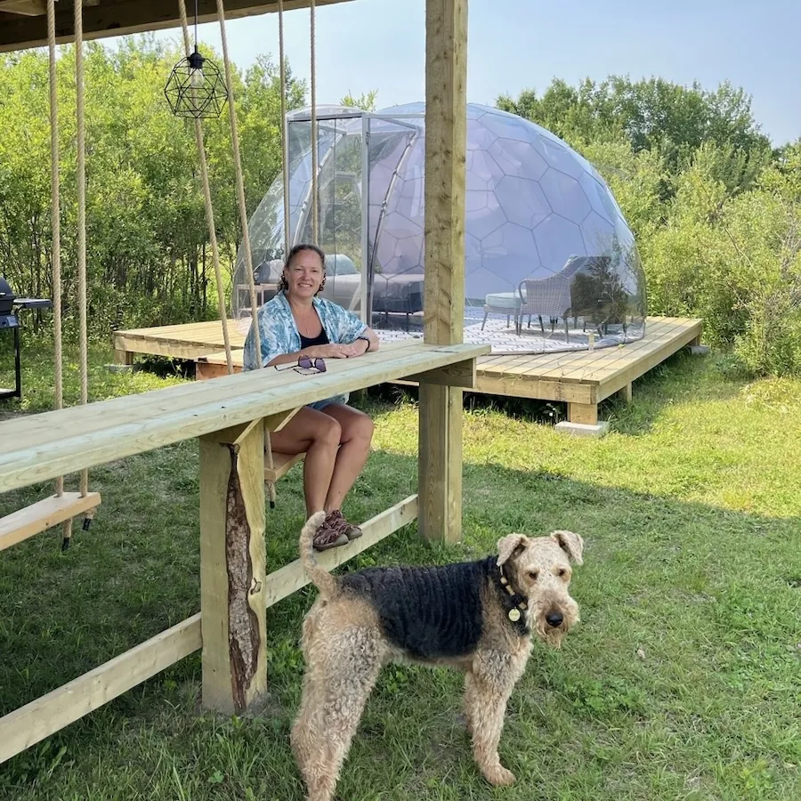 A woman sitting in front of a geodesic off-grid dome