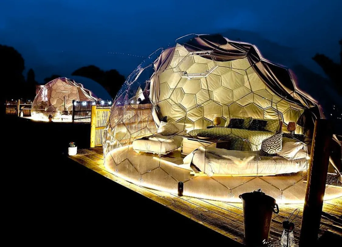 Interior of a modern glamping dome with bed, seating area, and panoramic window