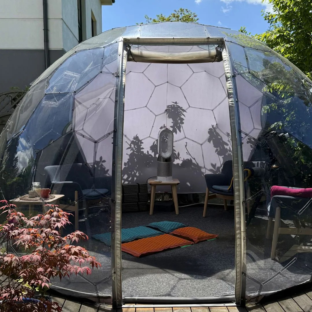 Close-up of an orange Pranamat ECO acupressure mat, with a Hypedome visible in the garden behind