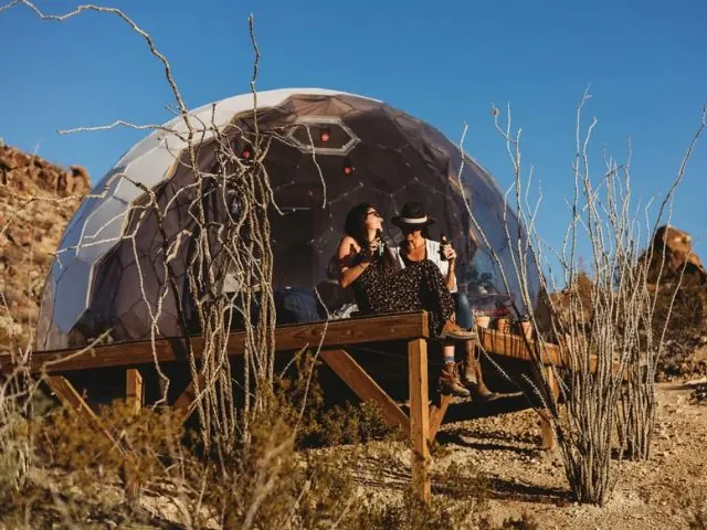 Two guests sitting on the deck of a Hypedome glamping dome at sunset in the Texas desert near Terlingua