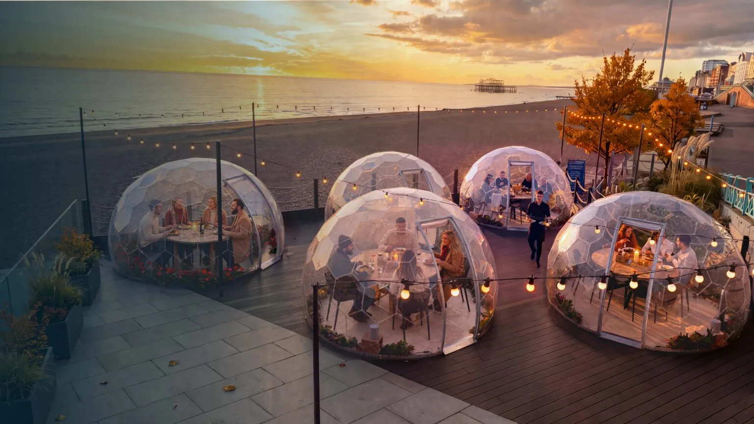 Dining Hypedomes on a seaside terrace at sunset, guests dining inside
